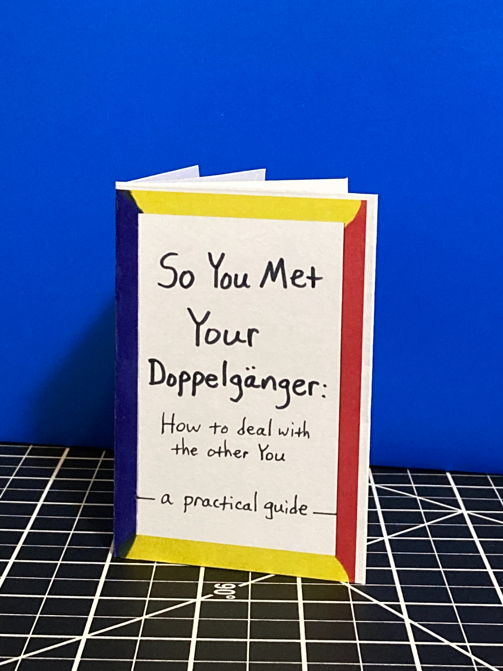 A hand holds a mini zine titled So You Met Your Doppelganger